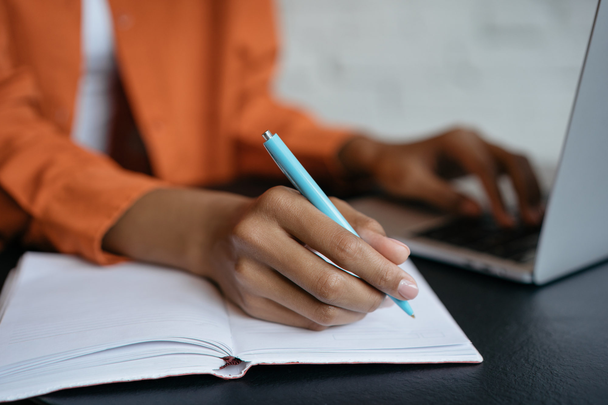 Close-up shot of student hand holding pen and writing in notebook, working at home. E-learning